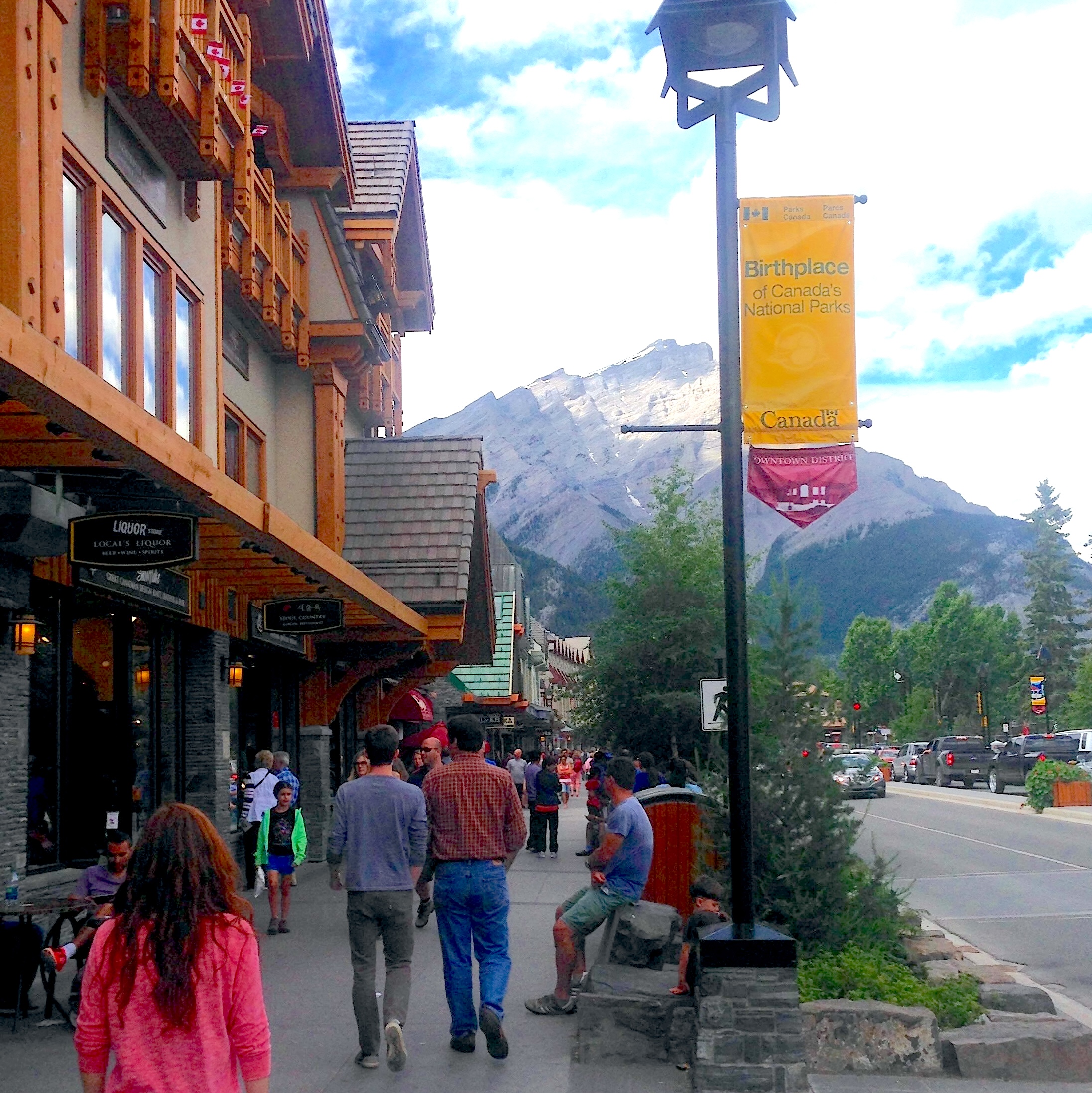 downtown Banff with people walking the sidewalks and the mountains in the background